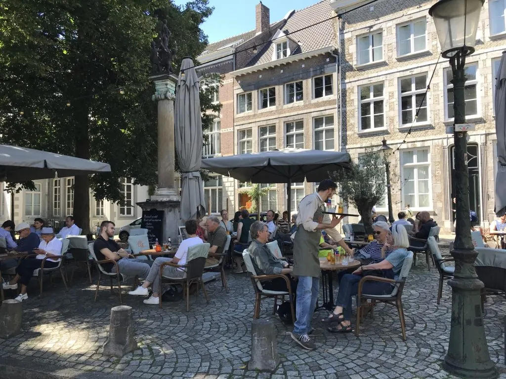 Terrasse animée du Restobar LURE sur la place du Jekerkwartier à Maastricht, avec un serveur qui apporte les boissons